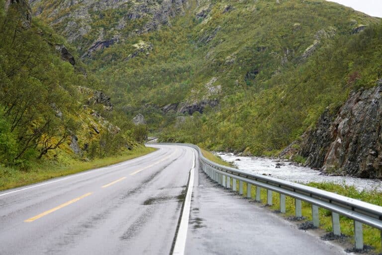 Een close-up van een weg langs een riviertje en bergen