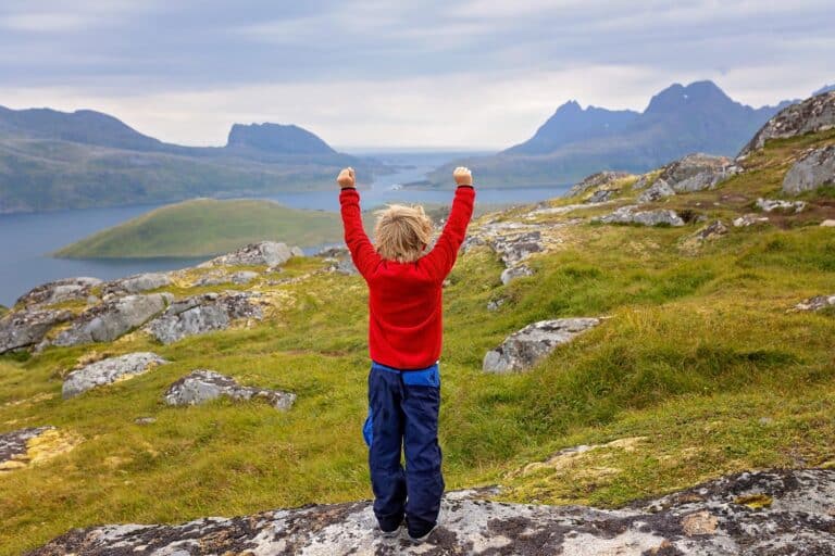 Blij kind tijdens het wandelen, uitkijkend over de bergen en water