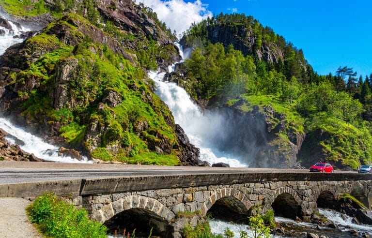 Twee auto's die de Låtefoss passeren over een lage brug langs de waterval