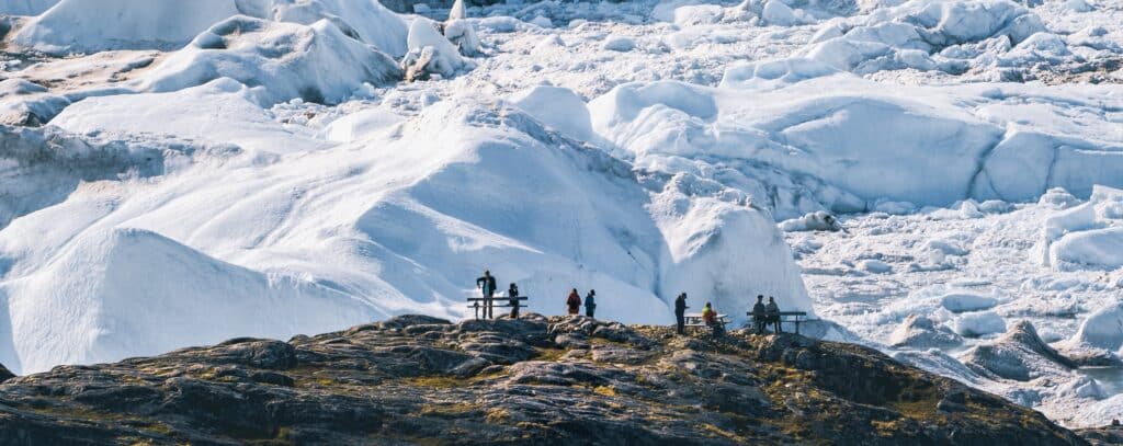 Mensen zitten aan picknicktafels voor een gletsjerwand van de Eqi gletsjer in Groenland