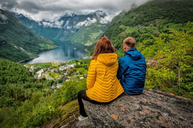 Stel kijkt zittend op een rots uit over het Geirangerfjord in Noorwegen