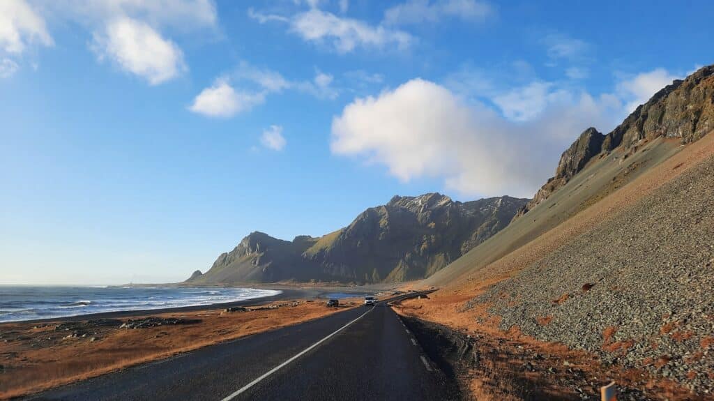 Weg op IJsland langs de kust, met blauwe lucht en bergen op de achtergrond