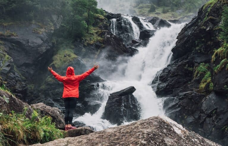 Vrouw met rode jas staat voor Latefossen waterval in Noorwegen