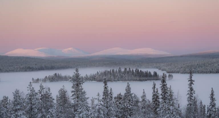 Uitzicht over besneeuwde vallei met roze gloed in de lucht