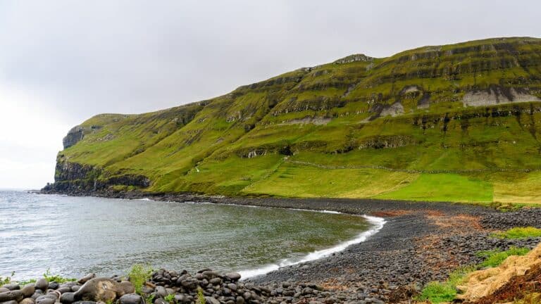 Strand met groene berg op de achtergrond op het eiland Sandoy, Faeröer eilanden