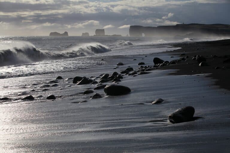 Zwart strand Rejnisfjara op IJsland, met op de achtergrond de rotsen van Dyrholaey