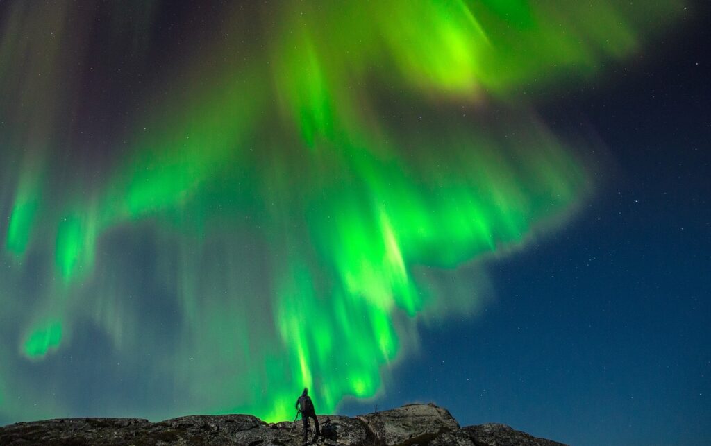 Noorderlicht in de donkere lucht, boven een man op een berg