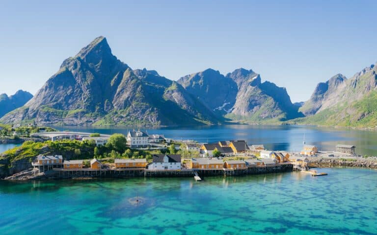 Zicht op geel dorpje op de Lofoten, omgeven door spitse bergen en helderblauw zeewater