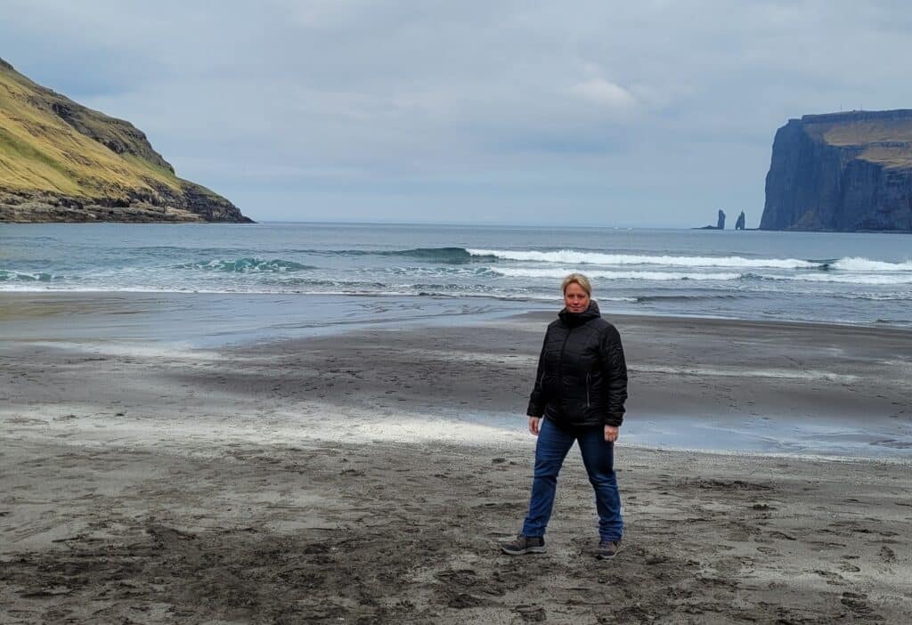 Vrouw staat op het strand van Tjornuvik, Faeröer eilanden.