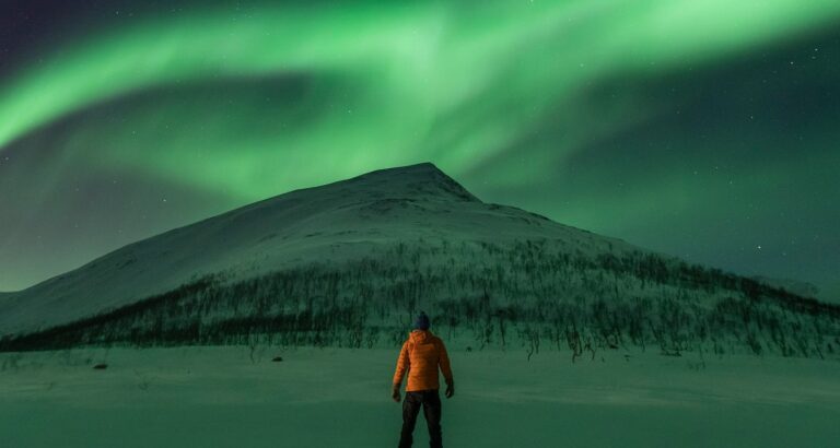 Man uitkijkend over berg in Noorwegen met noorderlicht