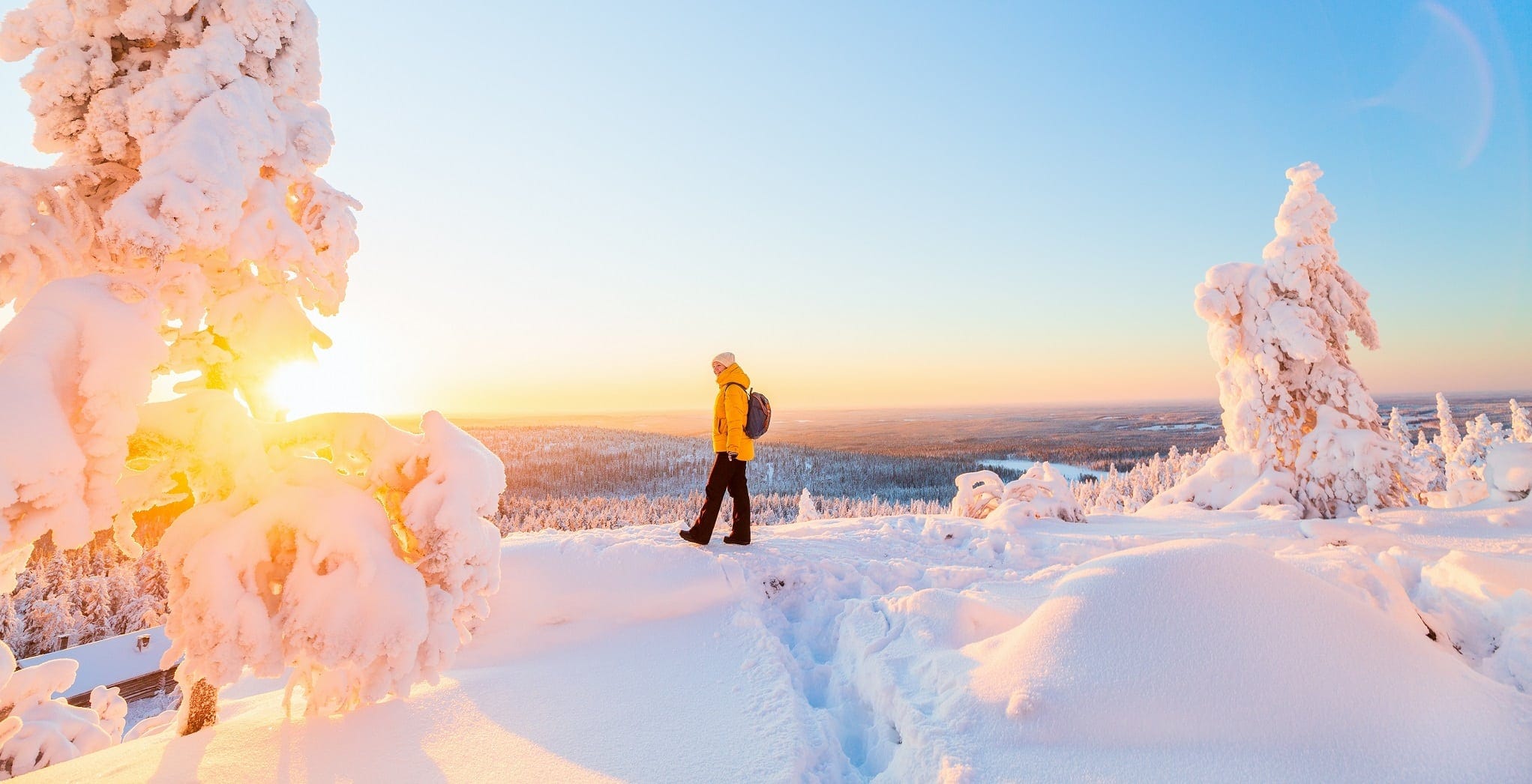 Vrouw in gele jas kijkt naar zonsondergang in sneeuwlandschap Lapland.