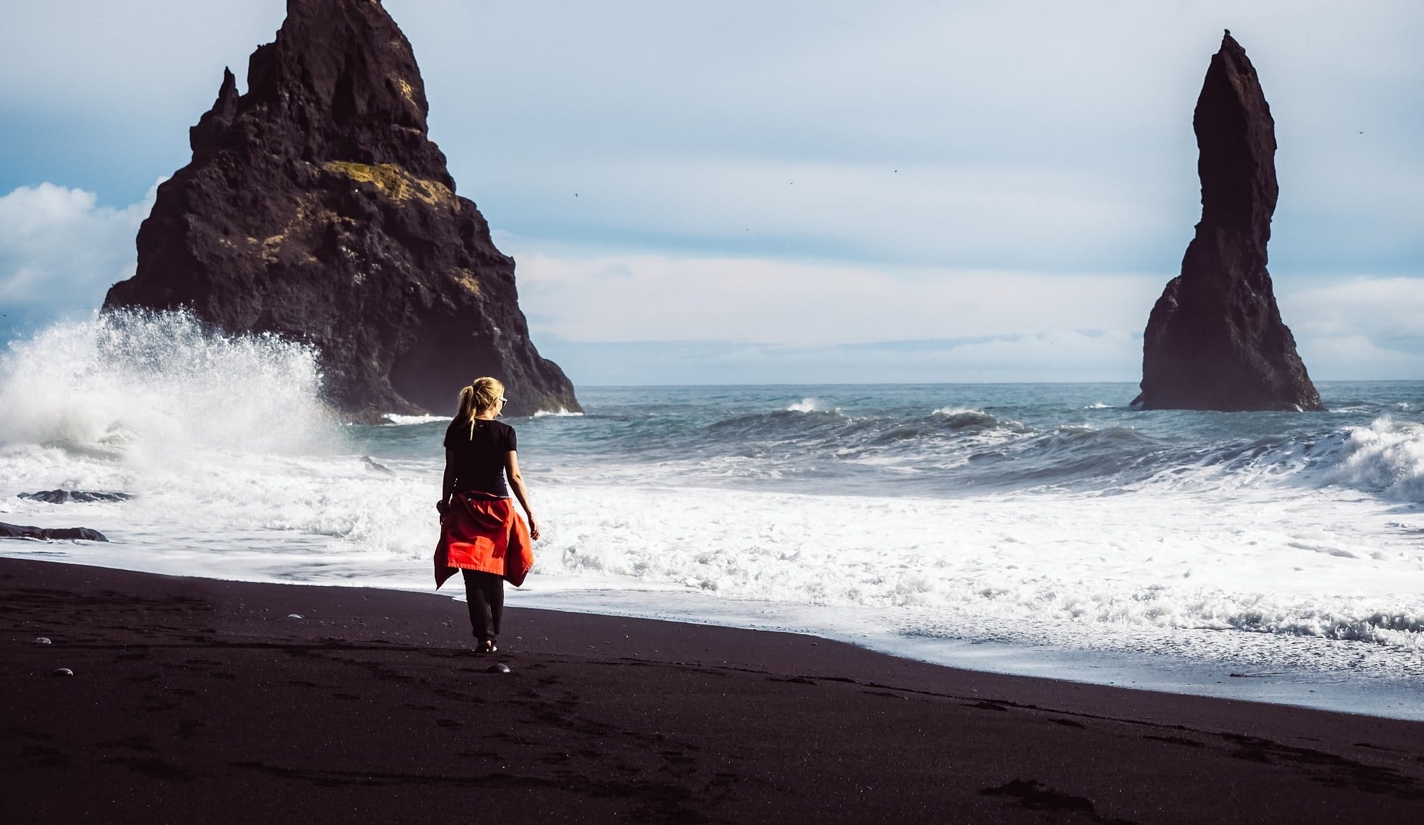 Vrouw loopt over zwart strand in IJsland