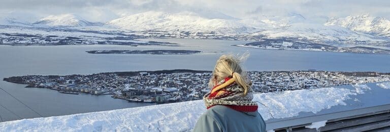 Vrouw kijkt uit over Tromso vanaf uitkijkpunt.