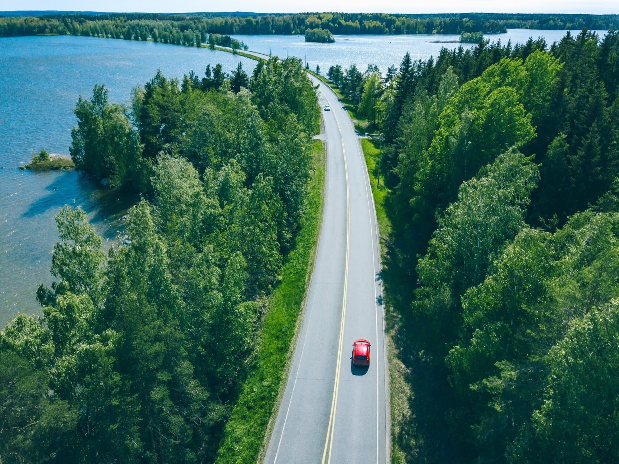 Luchtfoto van rode auto die langs een meer in Zweden rijdt.