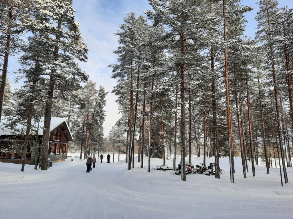 Mensen lopen over besneeuwd pad bij hoofdgebouw Himmerki Lodge, Fins Lapland