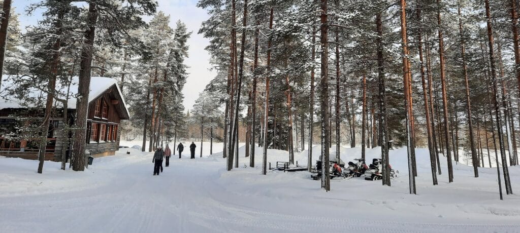 Mensen lopen over besneeuwd pad bij hoofdgebouw Himmerki Lodge, Lapland