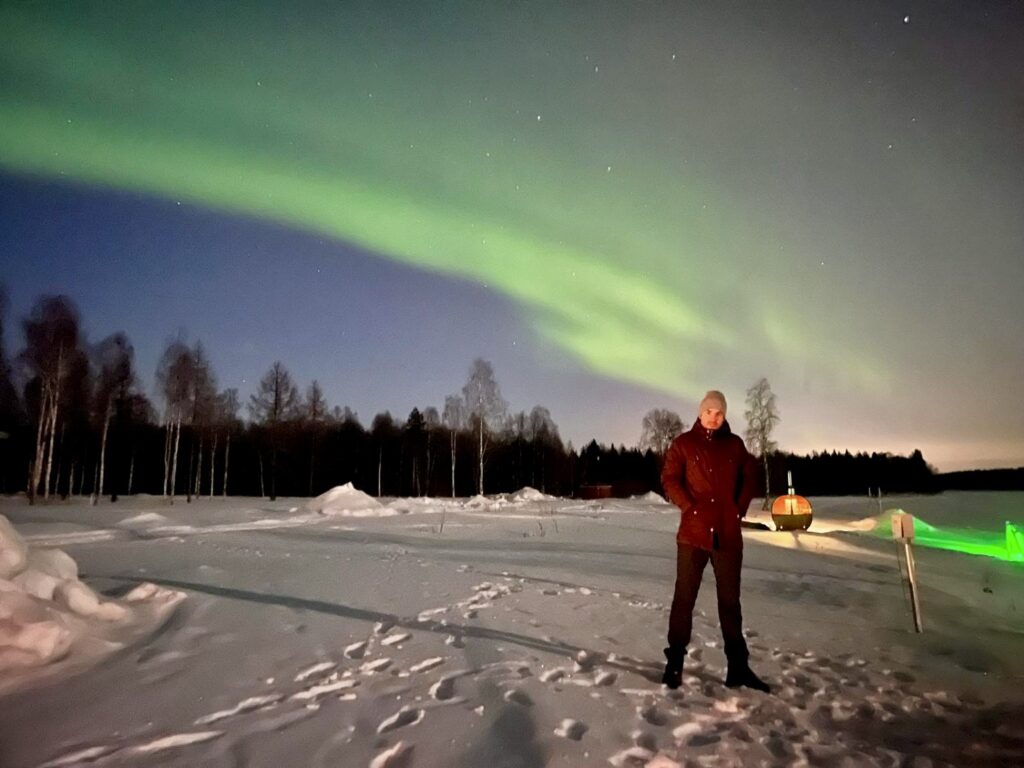 Man poseert voor het noorderlicht in de sneeuw van Lapland