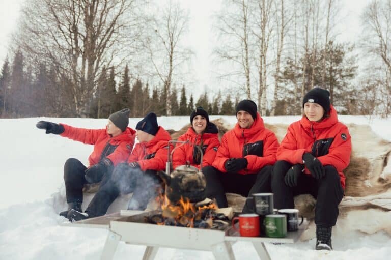 Mensen zitten in de sneeuw bij een kampvuur in Zweeds Lapland