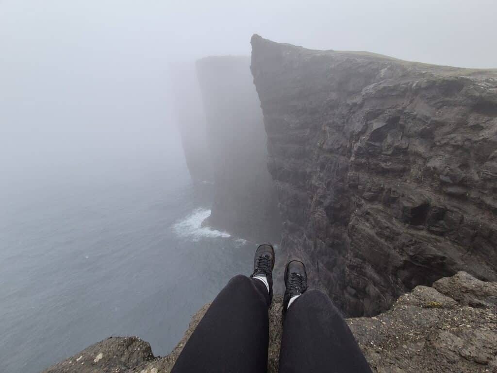 Voeten bungelen bij klif op de Faeröer eilanden.