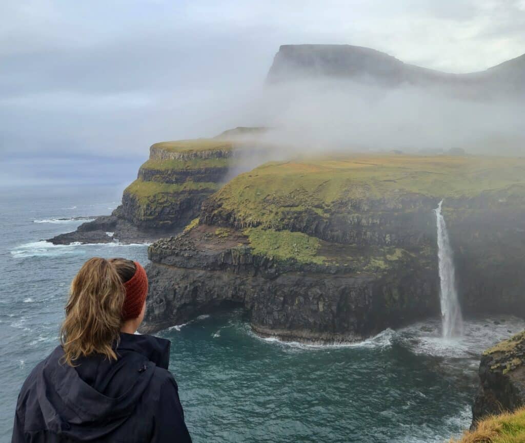Vrouw kijkt uit op Mulafossur op de Faeröer eilanden