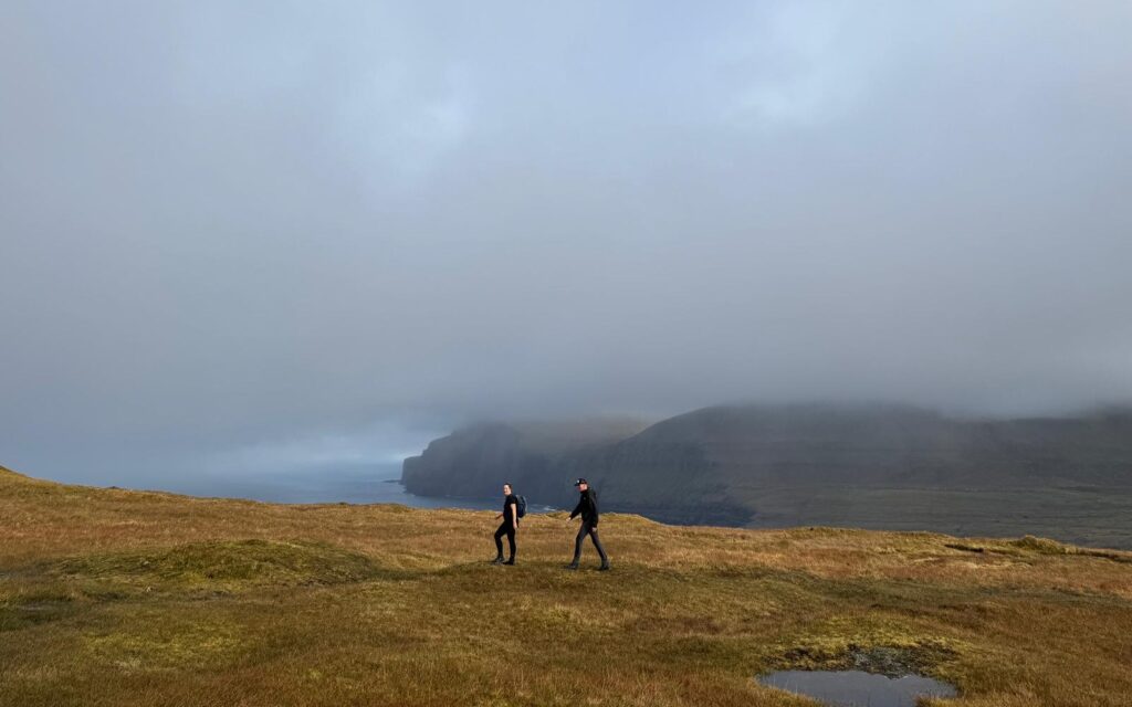 Twee wandelaars lopen langs de ruige kust van de Faeröer eilanden.