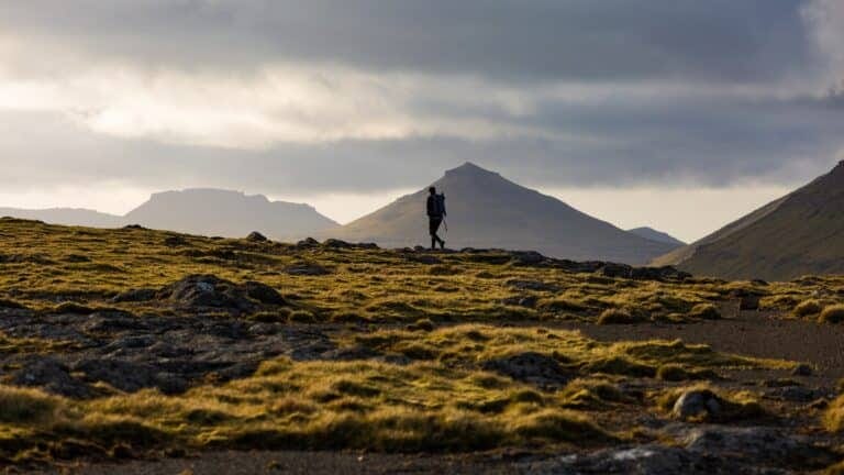 Wandelaar in de laagstaande zon op hoogvlakte met uitzicht op bergtoppen op de Faeröer eilanden