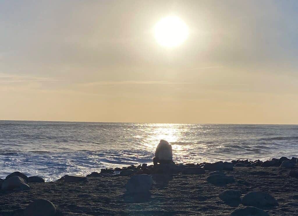 Man zit op steen, zwart strand Reynisfjara