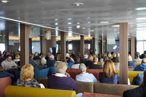 Mensen in de lounge van expeditie schip de Hondius luisteren aandachtig naar een lezing