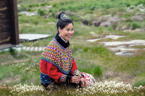 Jonge vrouw in Inuit kledij zittend op gras in Groenland