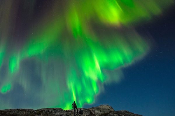 Noorderlicht in de donkere lucht, boven een man op een berg
