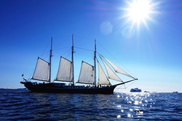 Zeilschip De Rembrandt op open water met her en der een ijsbergje, zonnige dag
