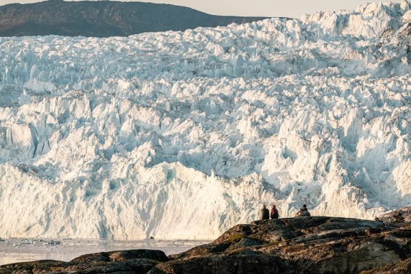 Mensen kijken zittend uit over de Eqi gletsjer in Groenland