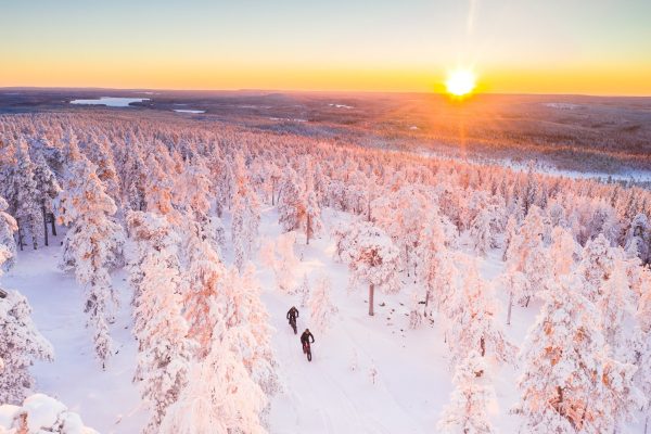 Luchtfoto van twee mensen op een fatbike in de sneeuw bij zonsondergang in Fins Lapland