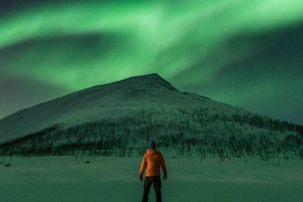 Man uitkijkend over berg in Noorwegen met noorderlicht