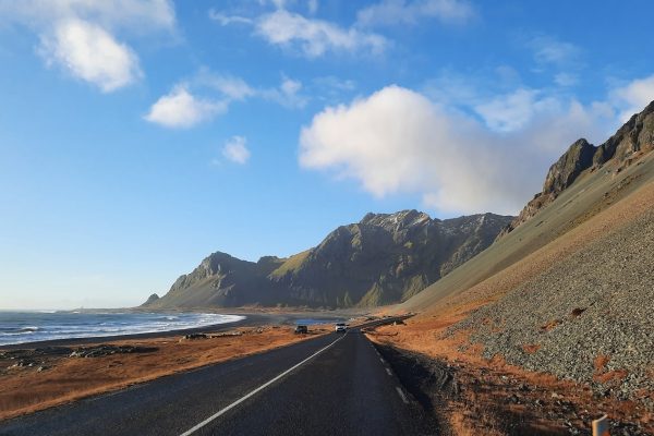 Weg op IJsland langs de kust, met blauwe lucht en bergen op de achtergrond