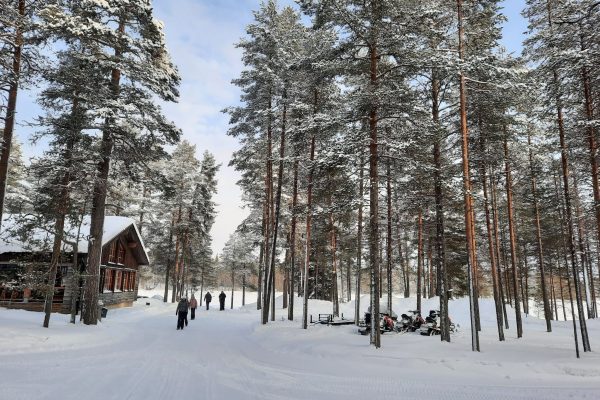 Mensen lopen over besneeuwd pad bij hoofdgebouw Himmerki Lodge, Fins Lapland