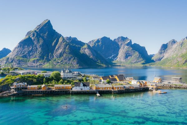 Zicht op geel dorpje op de Lofoten, omgeven door spitse bergen en helderblauw zeewater