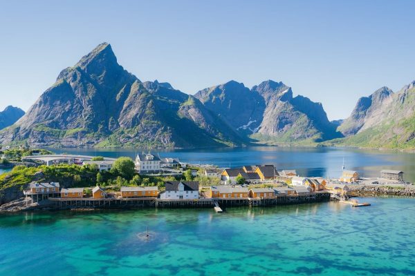 Zicht op geel dorpje op de Lofoten, omgeven door spitse bergen en helderblauw zeewater