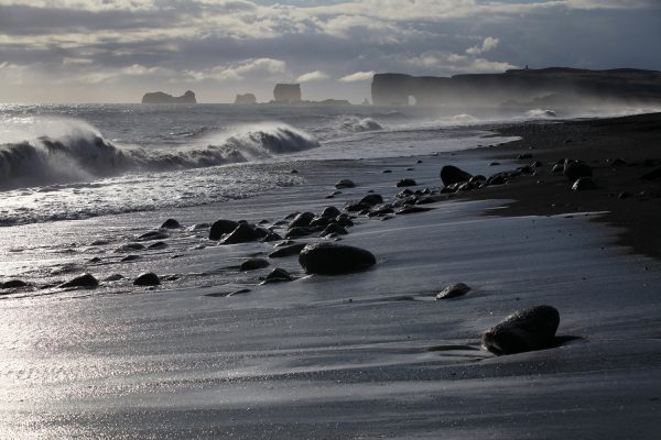Zwart strand Rejnisfjara op IJsland, met op de achtergrond de rotsen van Dyrholaey